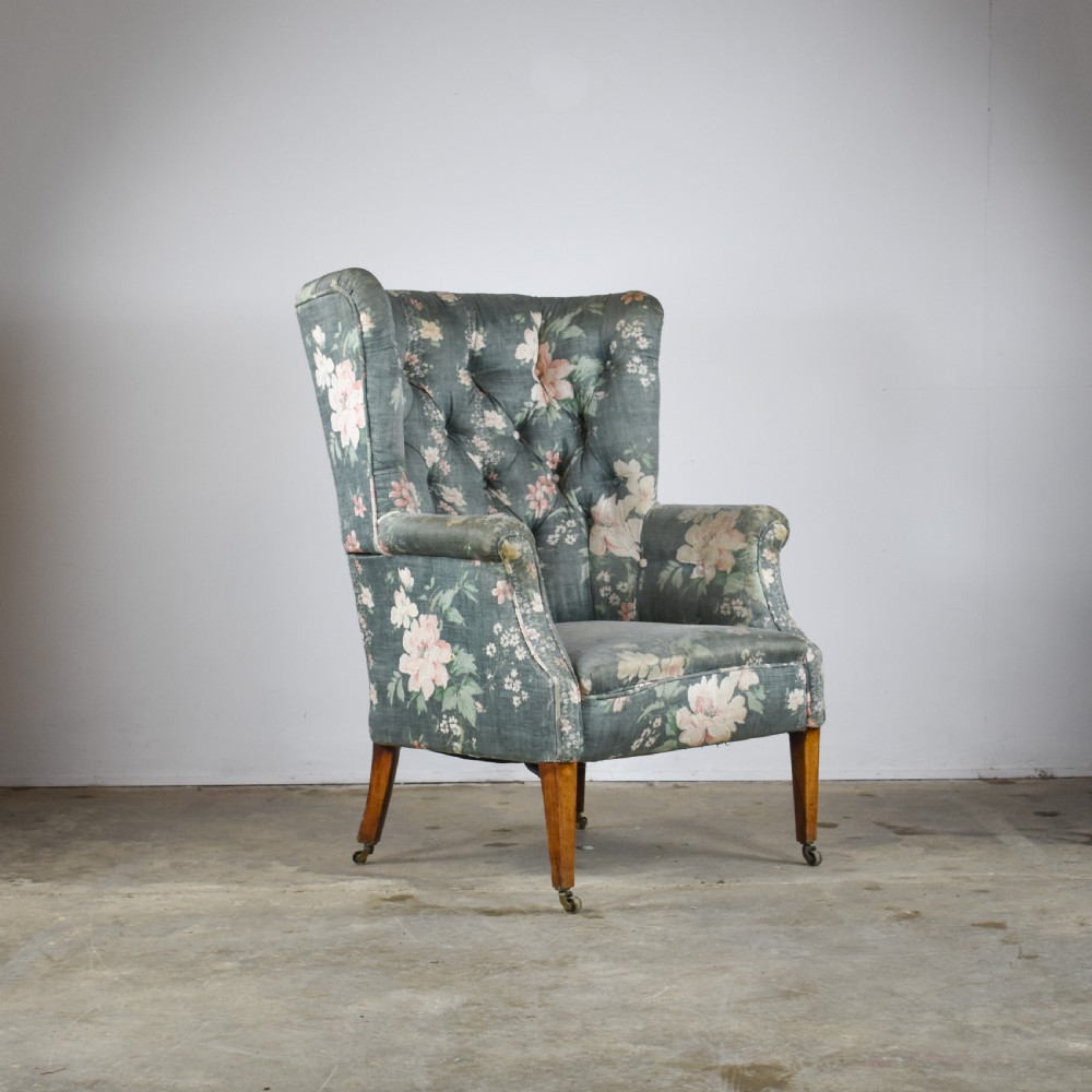 An Edwardian barrel back armchair upholstered in a green floral fabric with button tufting and tapered wood legs on brass castors.