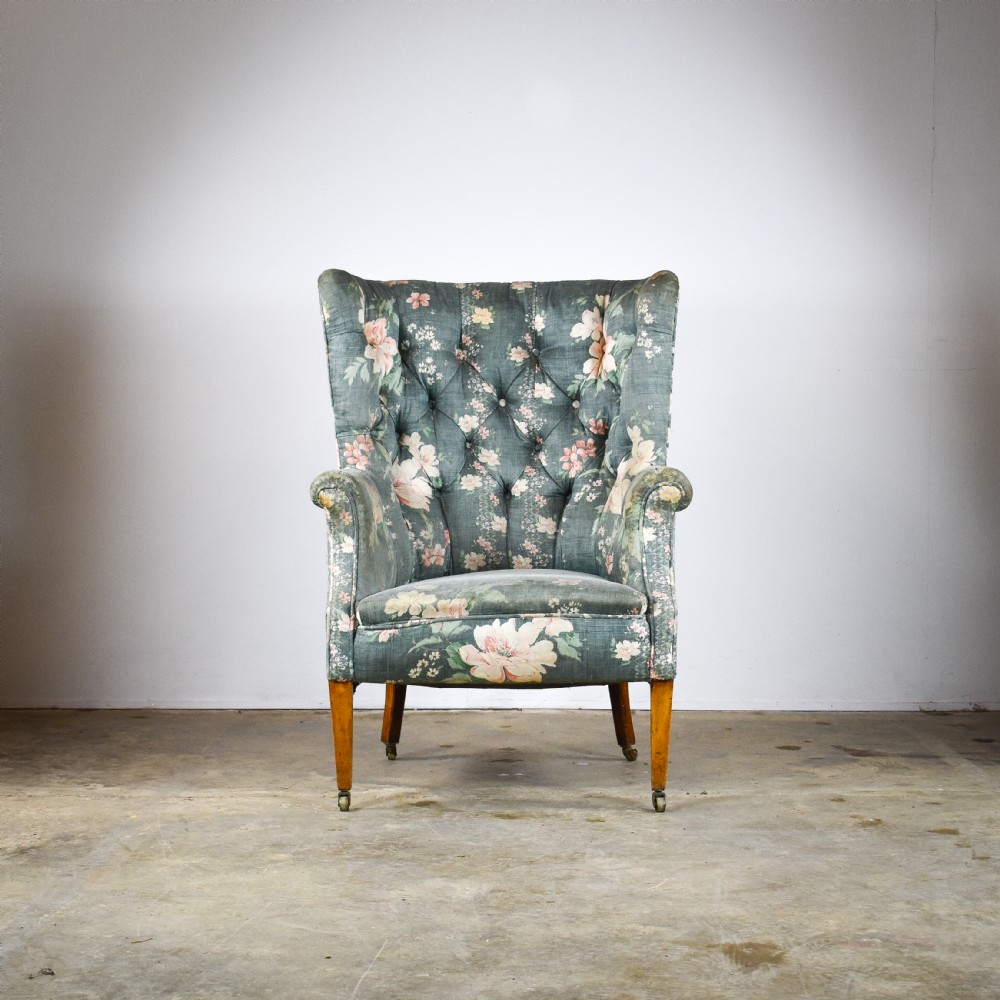 An Edwardian barrel back armchair upholstered in a green floral fabric with button tufting and tapered wood legs on brass castors. View II