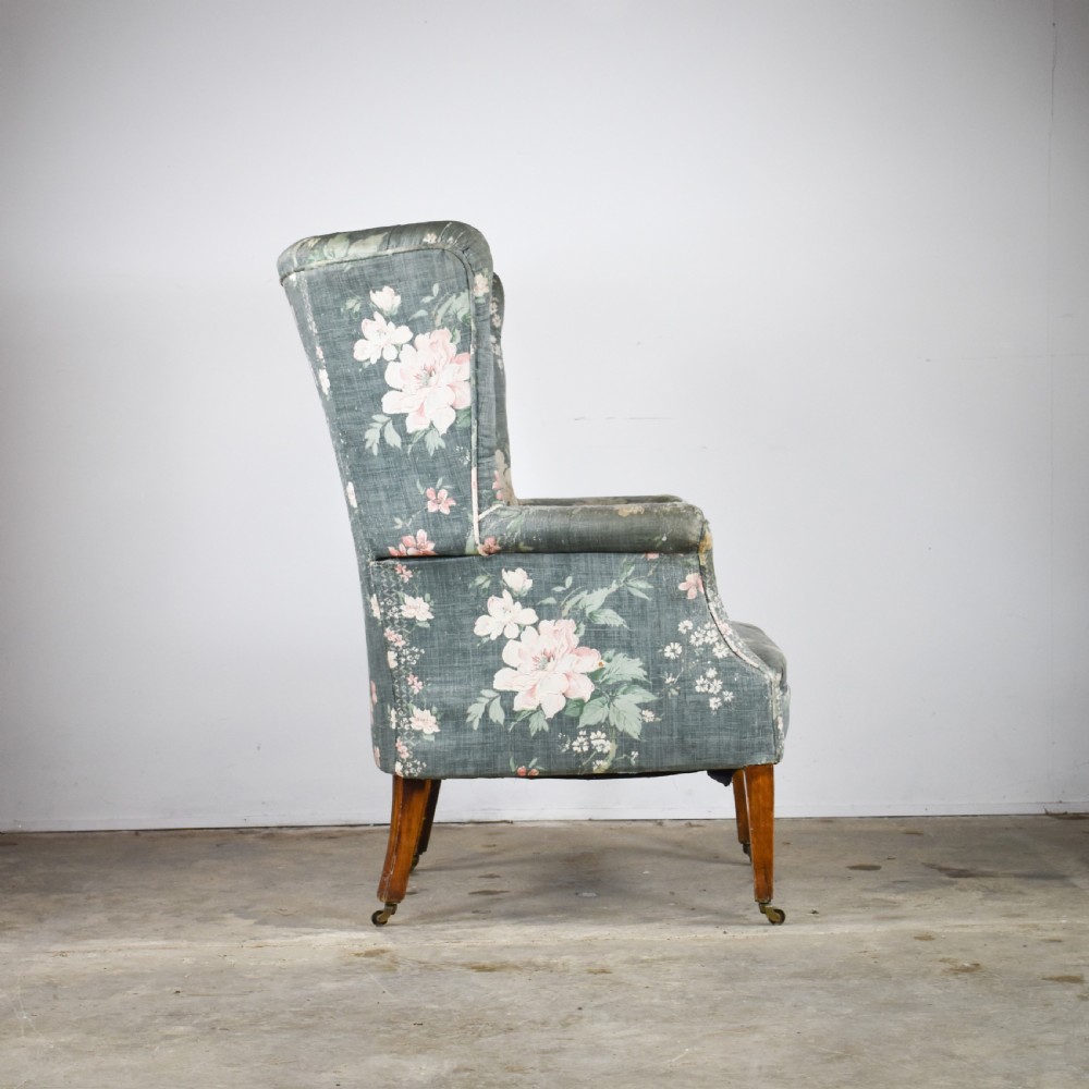 An Edwardian barrel back armchair upholstered in a green floral fabric with button tufting and tapered wood legs on brass castors. View III