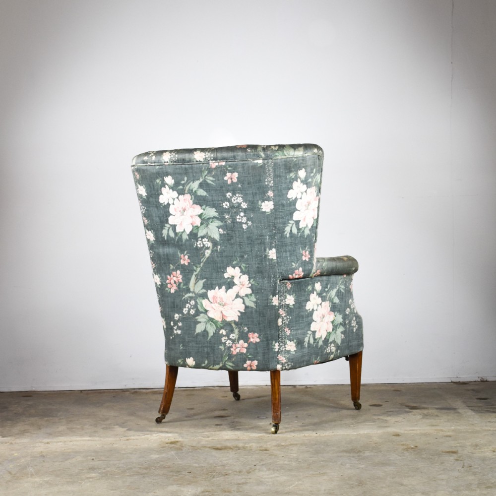 An Edwardian barrel back armchair upholstered in a green floral fabric with button tufting and tapered wood legs on brass castors. View IV