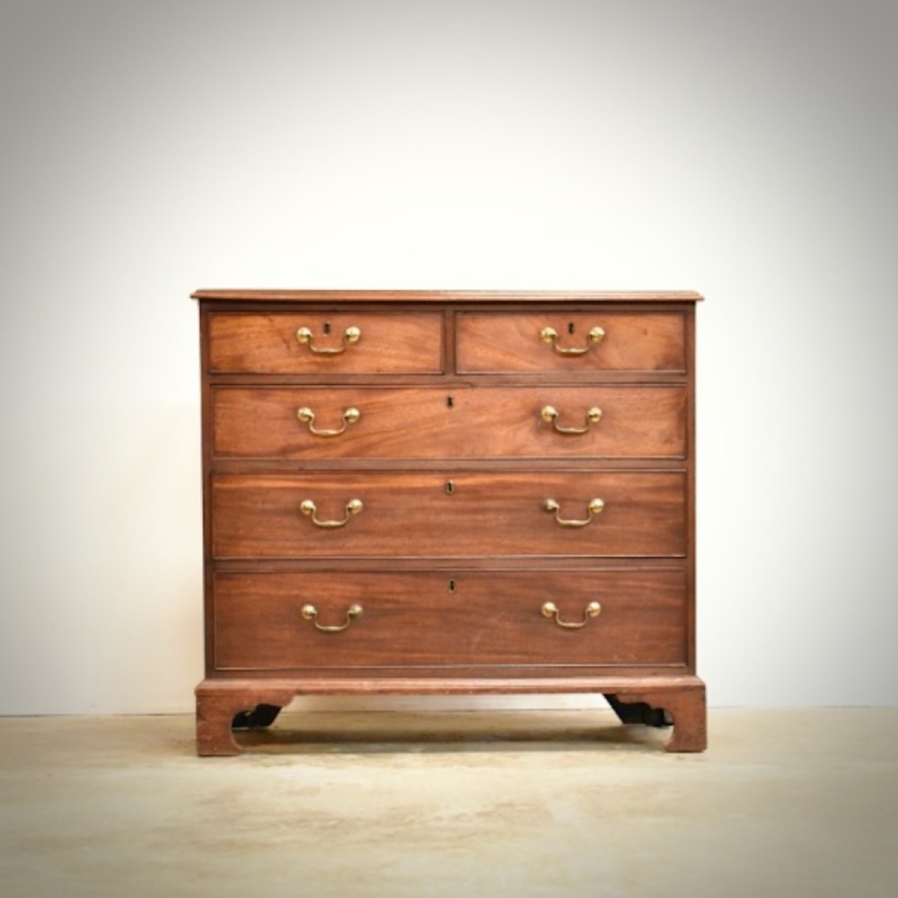 A George III mahogany chest of drawers featuring two short over three long drawers with brass swan-neck handles and bracket feet.
