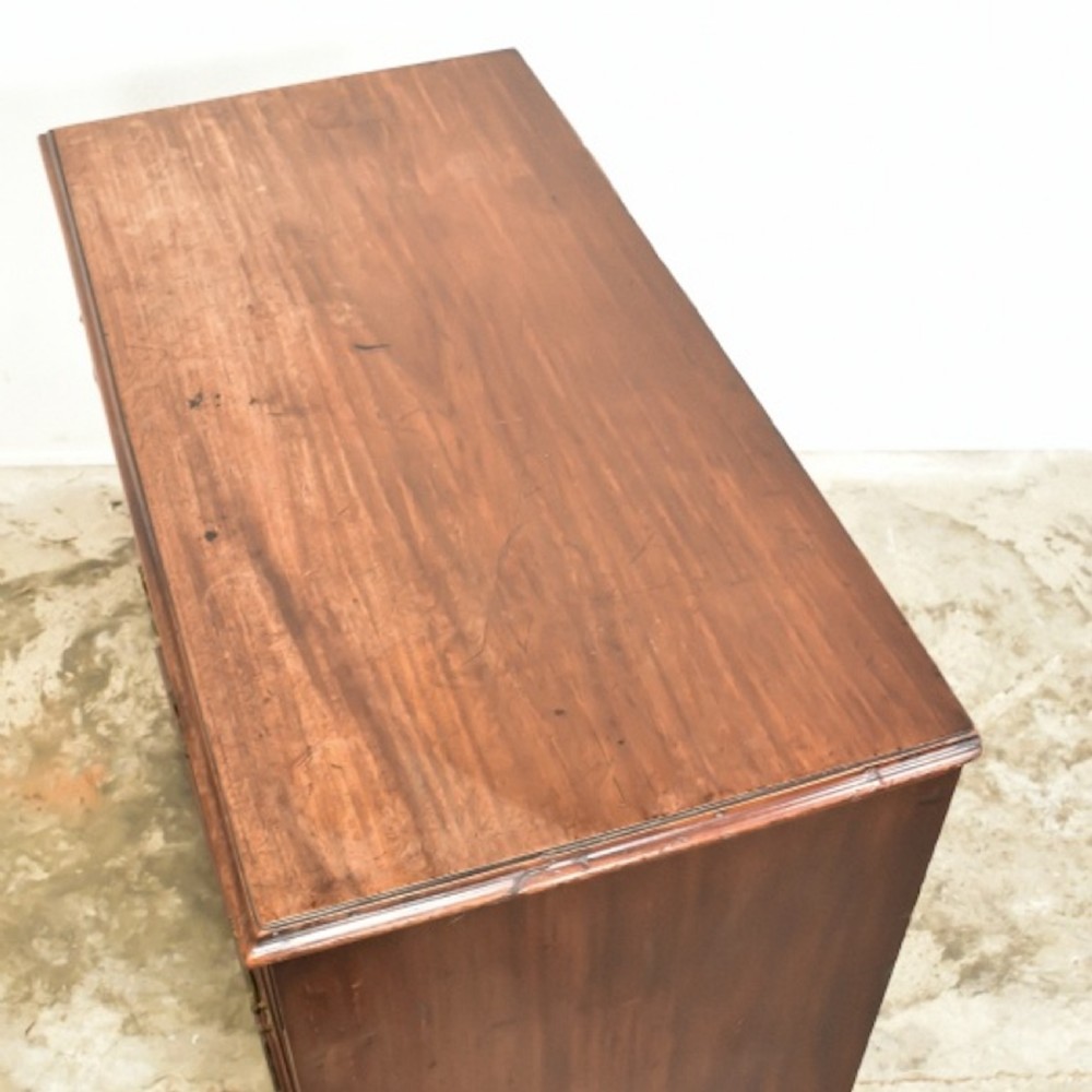 A George III mahogany chest of drawers featuring two short over three long drawers with brass swan-neck handles and bracket feet. View IV