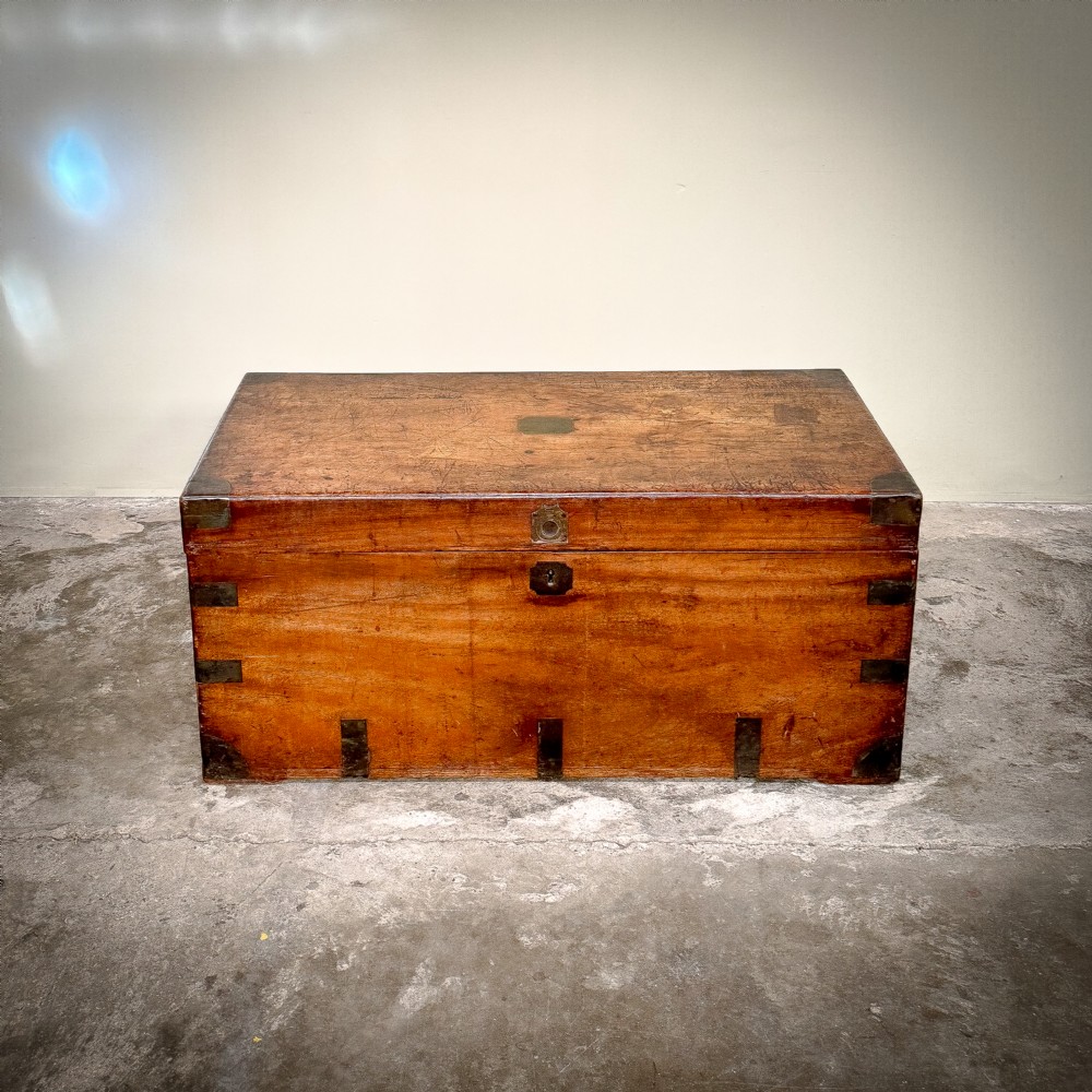A rectangular warm brown camphor wood trunk featuring flush brass corner brackets, strap mounts, and a central brass keyhole escutcheon.