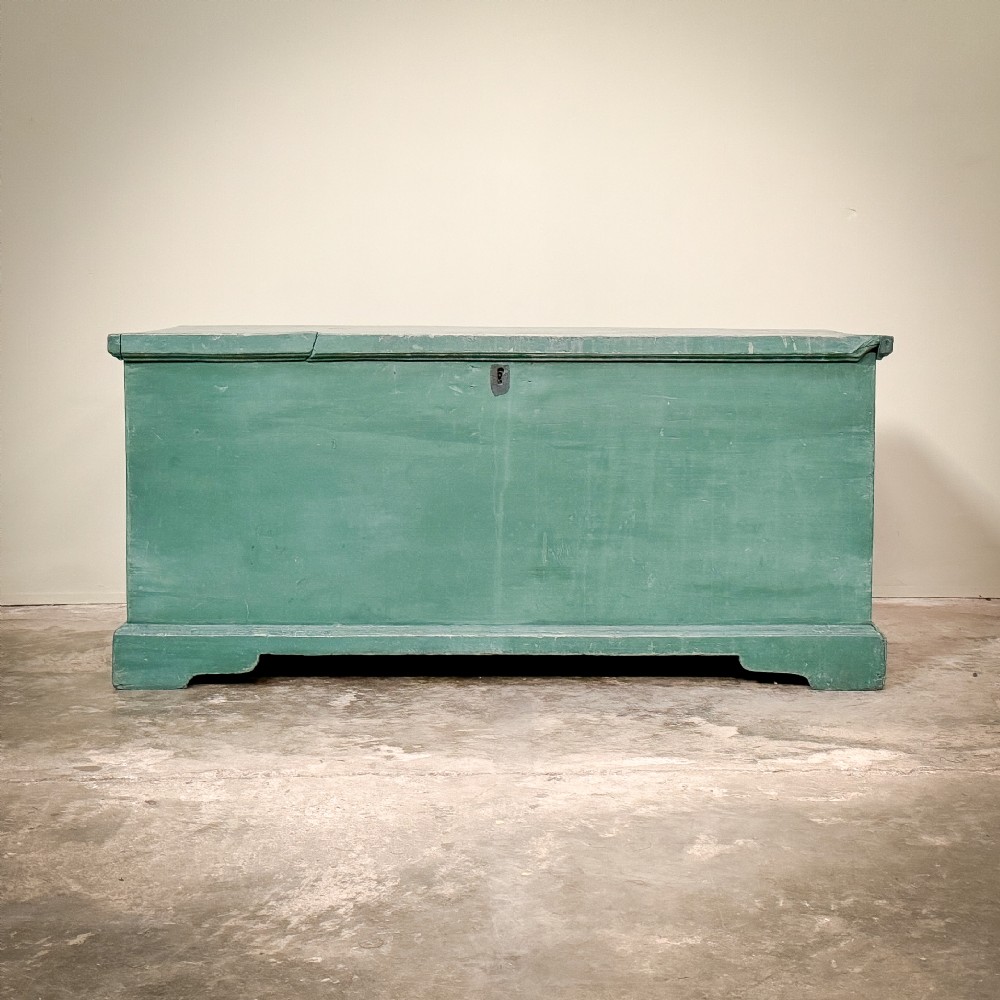 A large rectangular green painted pine blanket box with a flat hinged lid, a dark keyhole escutcheon, and a simple plinth base.