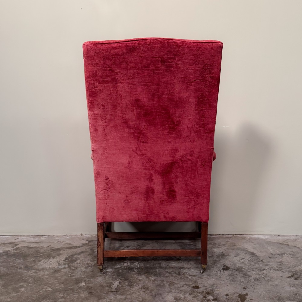 A classic English wingback armchair upholstered in red velvet with square timber legs, an H-stretcher base, and brass castors. View IV