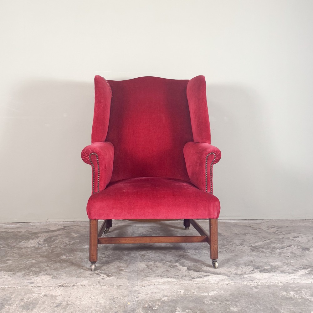 A 19th-century wingback armchair upholstered in red velvet with brass stud detailing on the arm fronts and timber legs on castors. View III