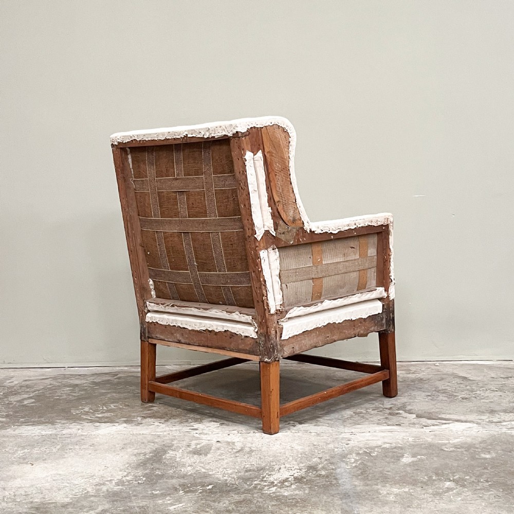 A 19th-century wingback armchair frame lined in cream calico fabric with exposed wooden side structure and square timber legs. View III