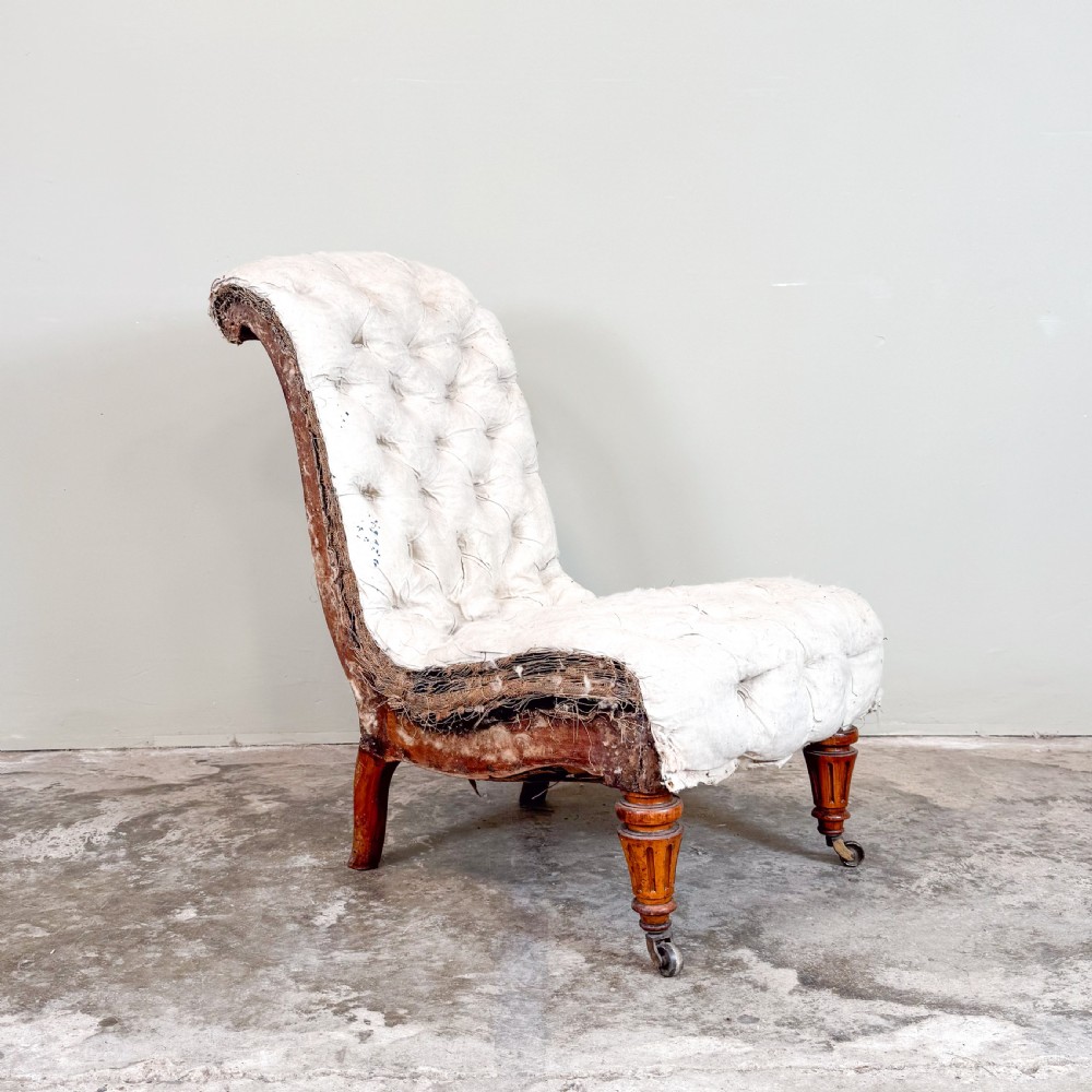 A Victorian armless slipper chair upholstered in off-white calico fabric with deep button-backed detailing and carved turned wooden legs on castors. View II