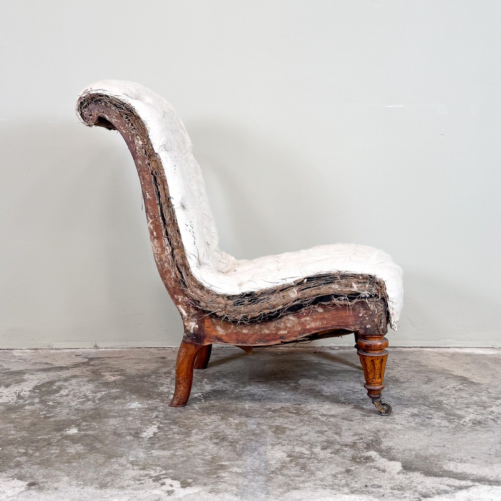 A Victorian armless slipper chair upholstered in off-white calico fabric with deep button-backed detailing and carved turned wooden legs on castors. View III