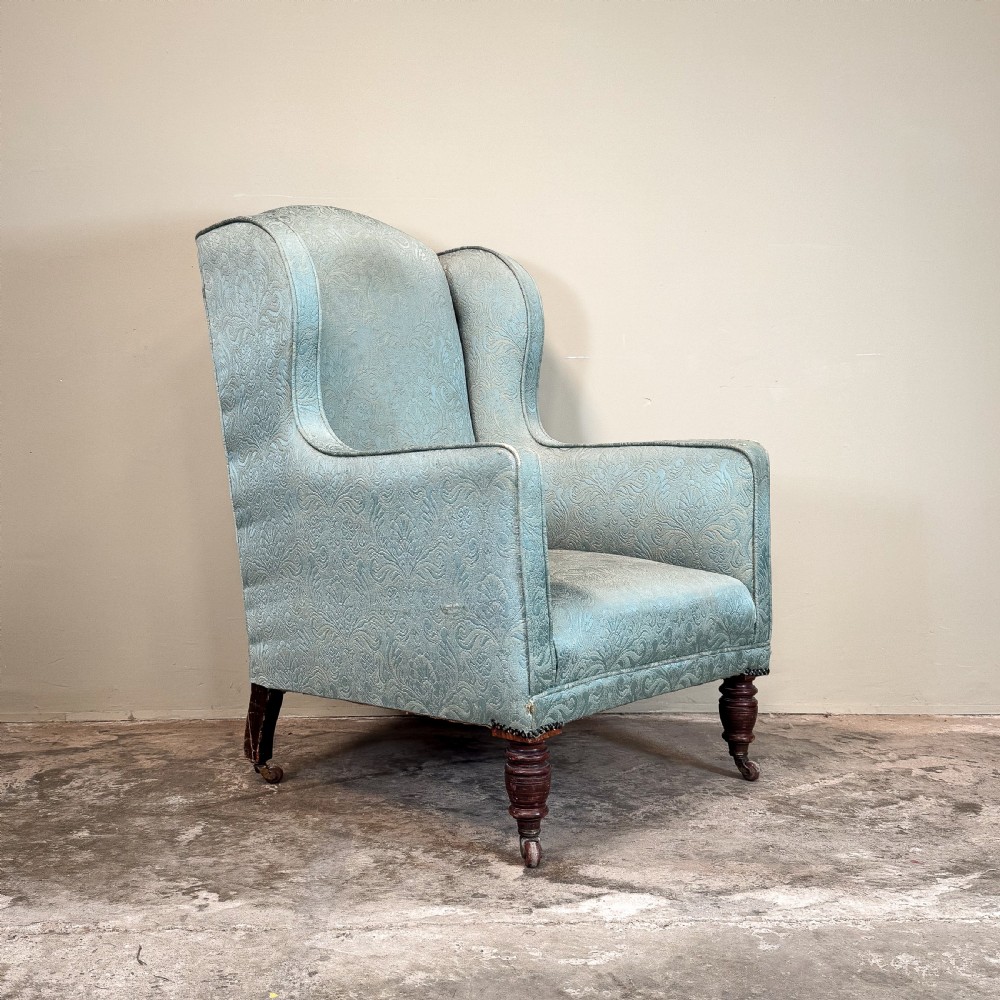 An Edwardian wingback armchair upholstered in duck egg blue patterned damask fabric with turned mahogany front legs on castors. View III
