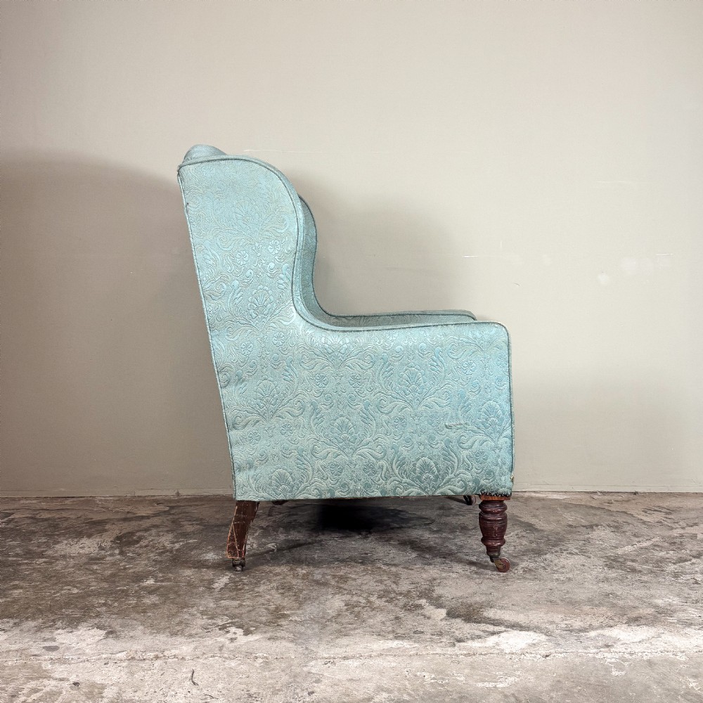 An Edwardian wingback armchair upholstered in duck egg blue patterned damask fabric with turned mahogany front legs on castors. View IV