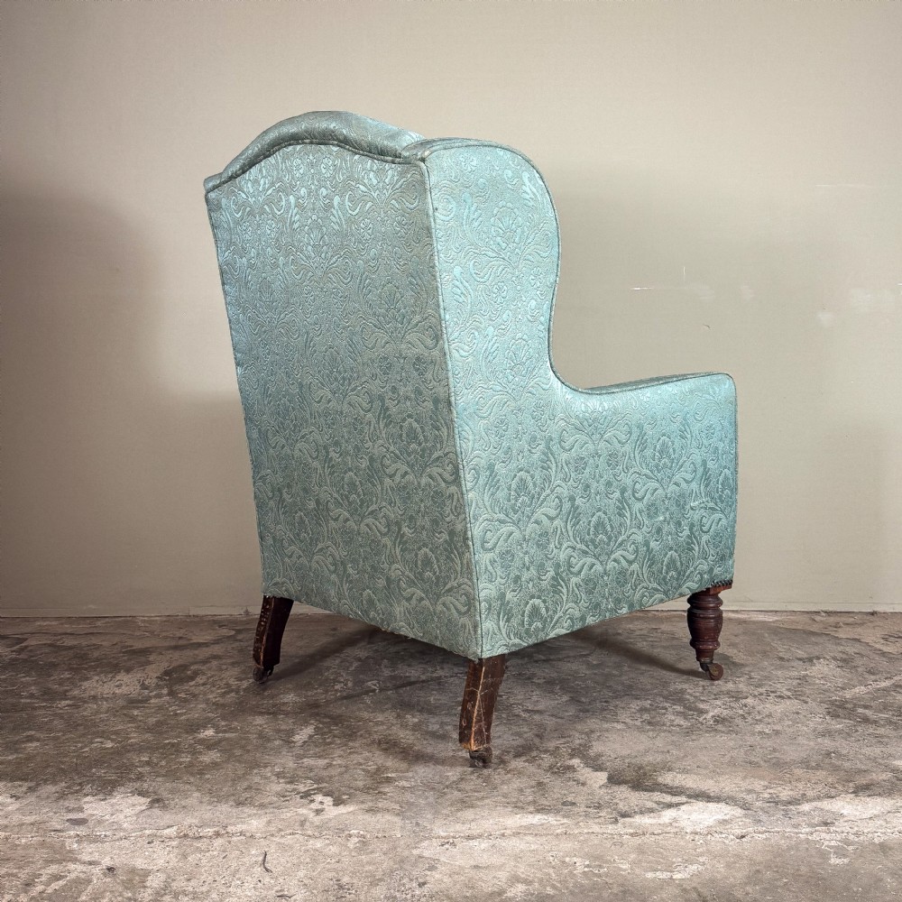 An Edwardian wingback armchair upholstered in duck egg blue patterned damask fabric with turned mahogany front legs on castors. View V