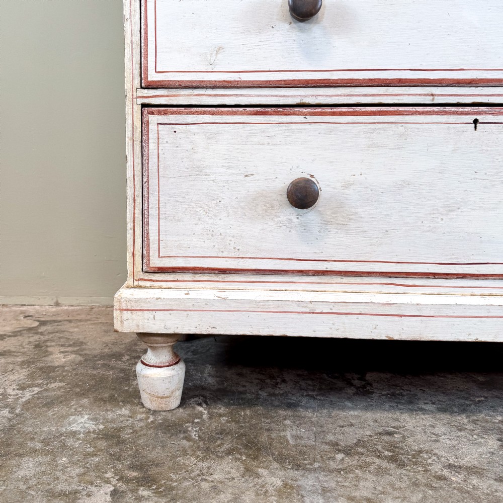 A 19th-century painted pine chest of drawers featuring five drawers with dark turned wooden knobs and red painted line details on an off-white background. View III