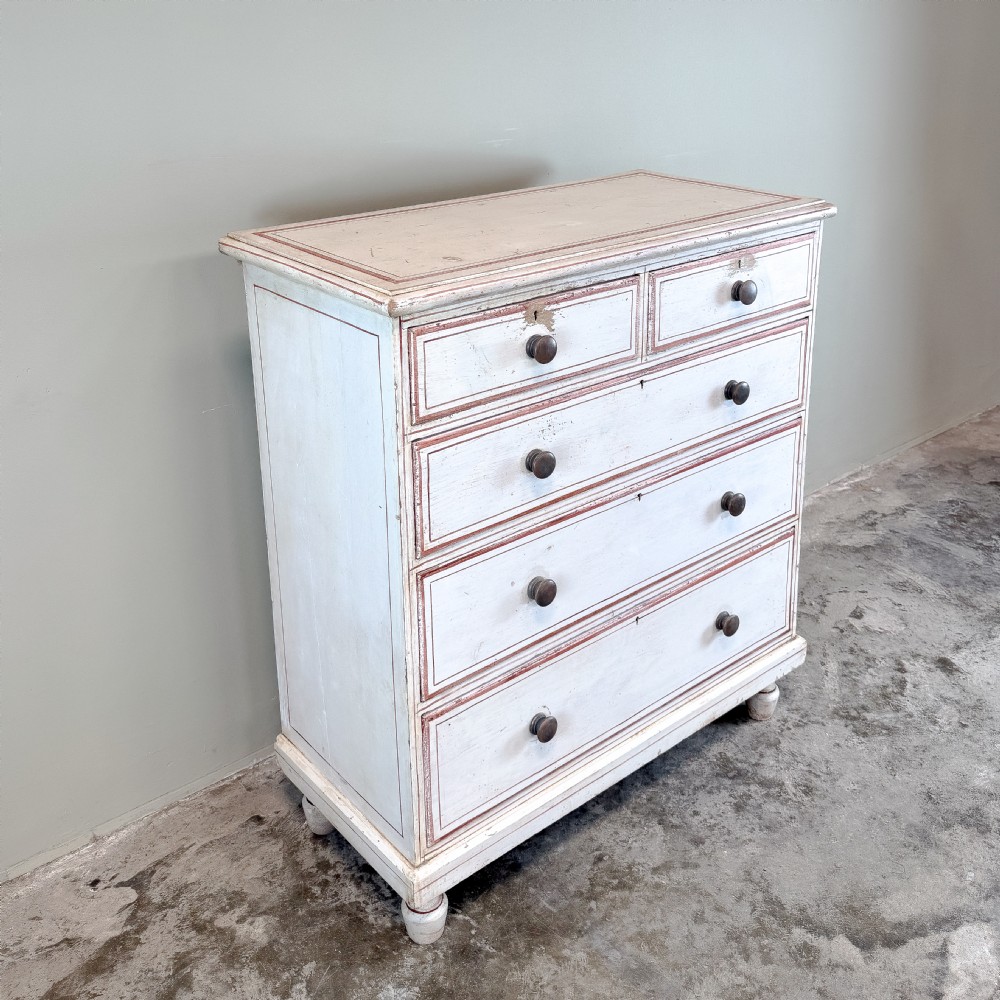 A 19th-century painted pine chest of drawers featuring five drawers with dark turned wooden knobs and red painted line details on an off-white background. View V