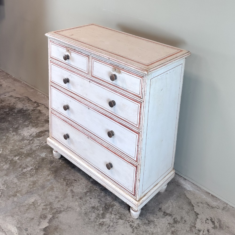 A 19th-century painted pine chest of drawers featuring five drawers with dark turned wooden knobs and red painted line details on an off-white background. View VI