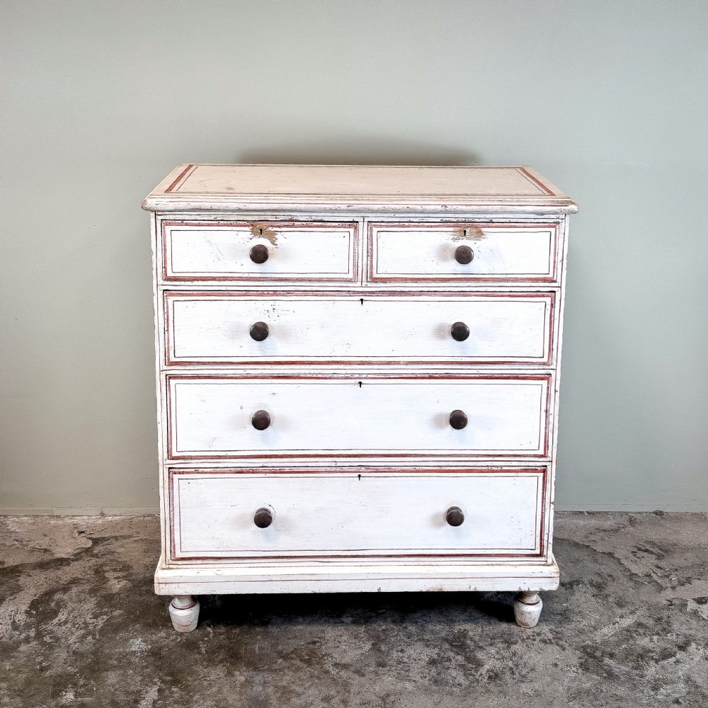 A 19th-century painted pine chest of drawers featuring five drawers with dark turned wooden knobs and red painted line details on an off-white background. View VII