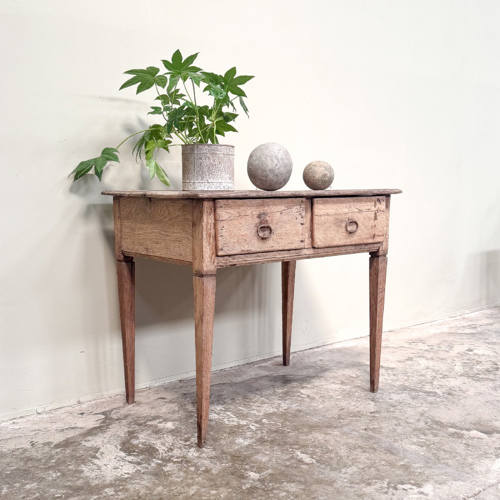 A rustic French side table crafted from weathered pale oak featuring two drawers with metal drop ring pull handles and square tapered legs. View II