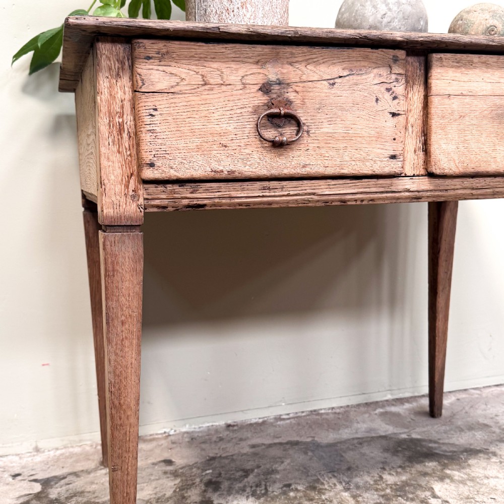 A rustic French side table crafted from weathered pale oak featuring two drawers with metal drop ring pull handles and square tapered legs. View III