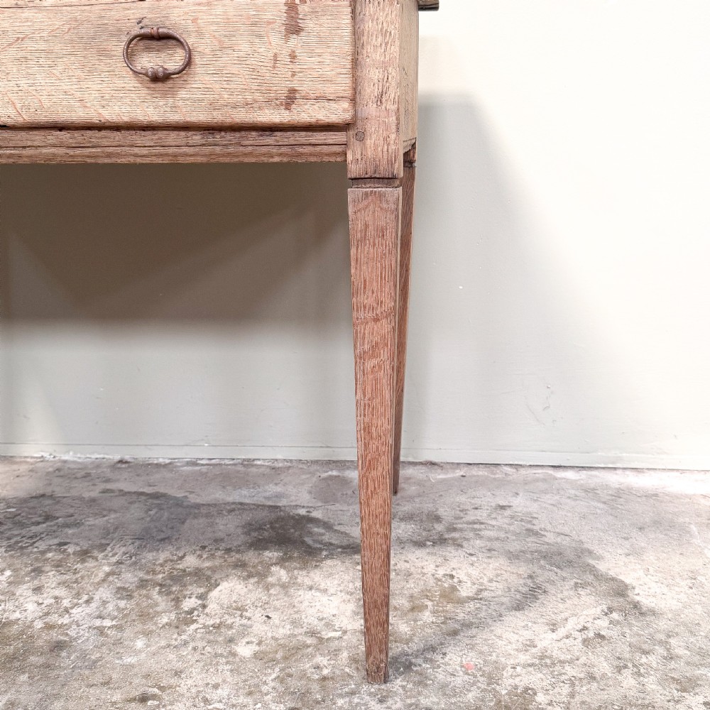 A rustic French side table crafted from weathered pale oak featuring two drawers with metal drop ring pull handles and square tapered legs. View IV