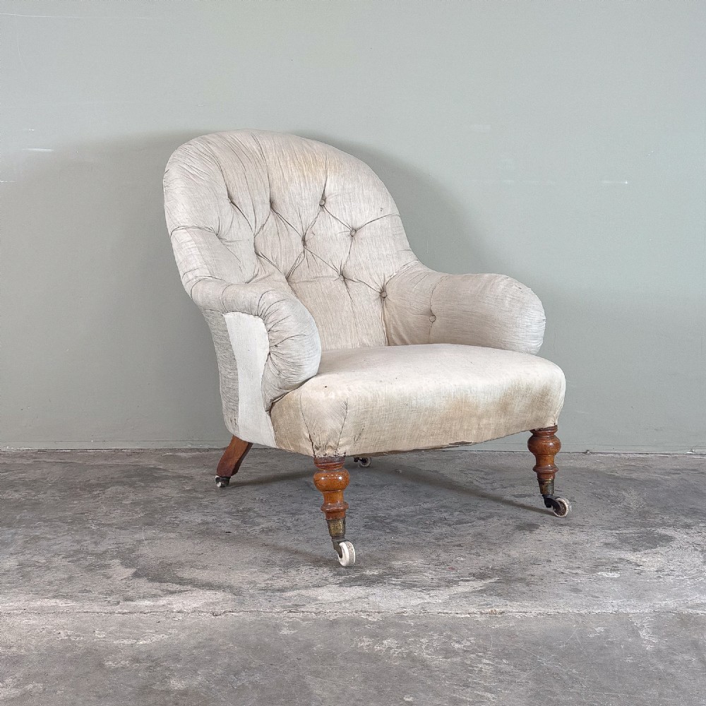 A 19th-century Victorian Howard style armchair upholstered in light cream fabric with deep button back tufting and turned wooden legs on brass castors. View II