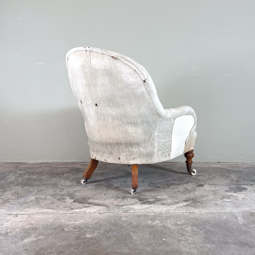 A 19th-century Victorian Howard style armchair upholstered in light cream fabric with deep button back tufting and turned wooden legs on brass castors. View V