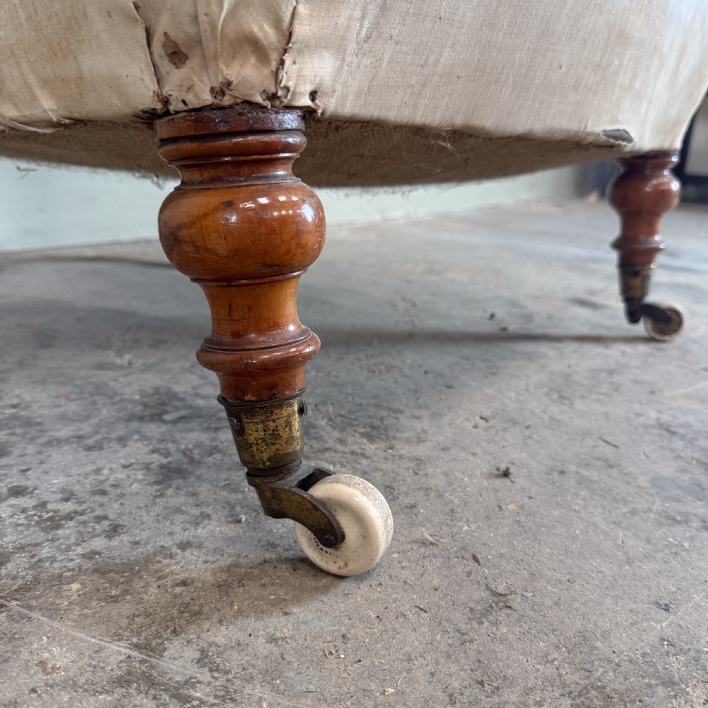 A 19th-century Victorian Howard style armchair upholstered in light cream fabric with deep button back tufting and turned wooden legs on brass castors. View VI