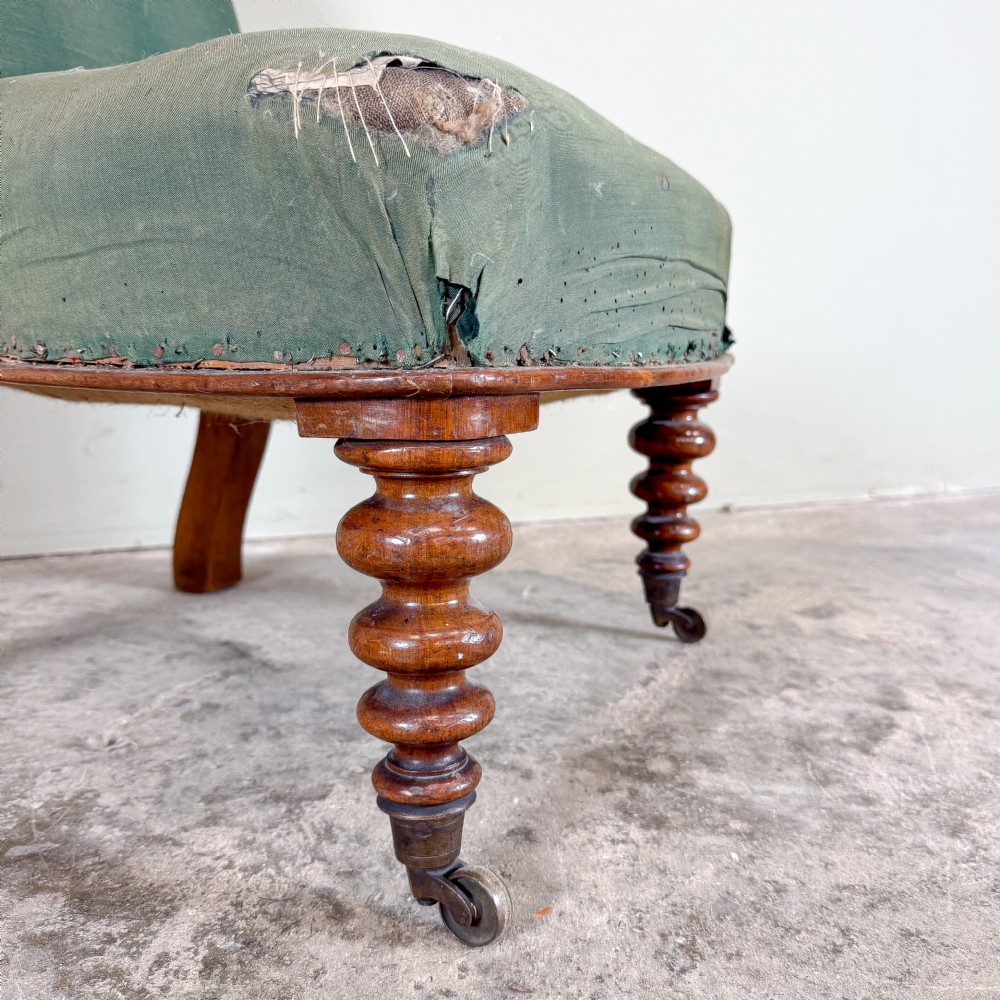 A low-seated Victorian armless slipper chair upholstered in green fabric featuring bobbin-turned wooden front legs on metal castors. View III