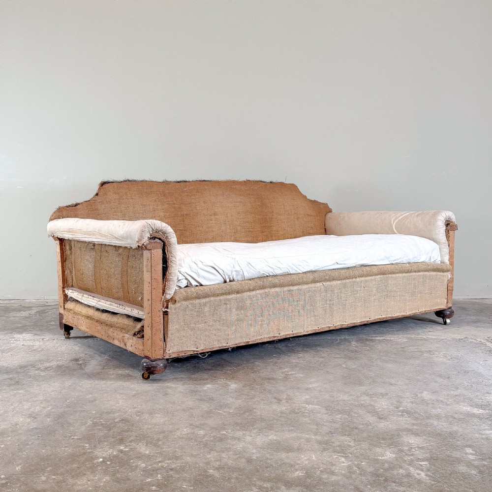 A 1930s deep-seated country house sofa frame upholstered in natural hessian and calico with turned wooden feet on brass castors.