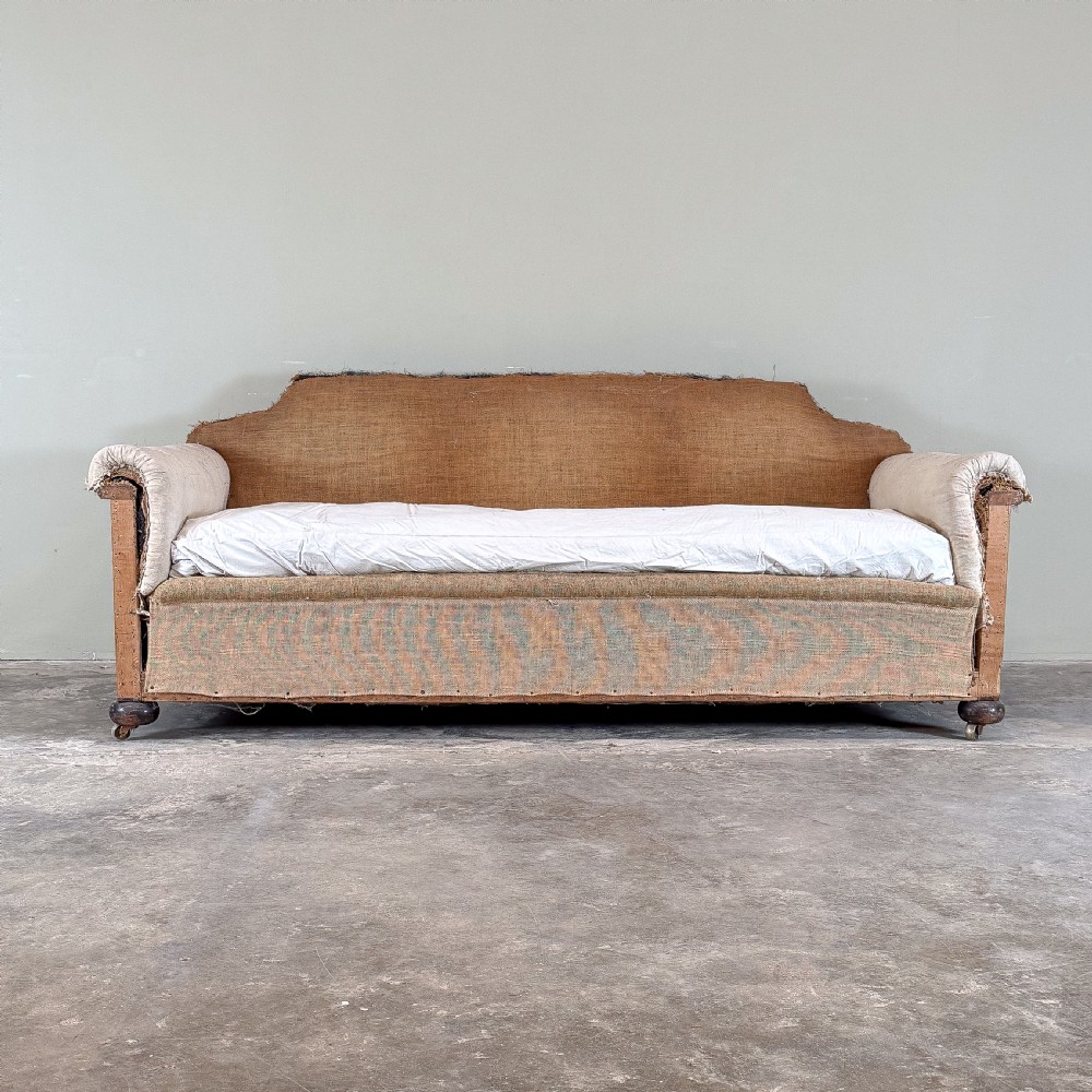A 1930s deep-seated country house sofa frame upholstered in natural hessian and calico with turned wooden feet on brass castors. View II