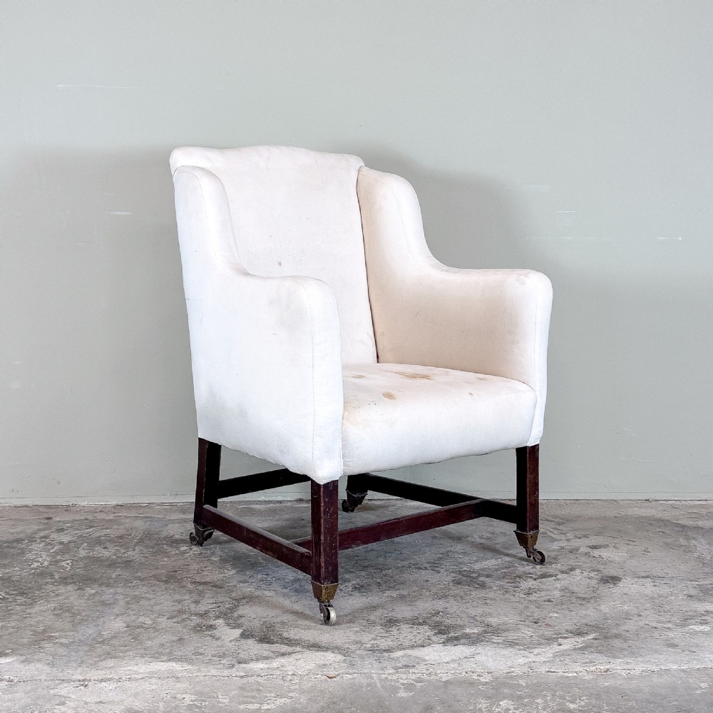An early nineteenth-century library armchair upholstered in off-white calico with dark mahogany legs and brass castors.