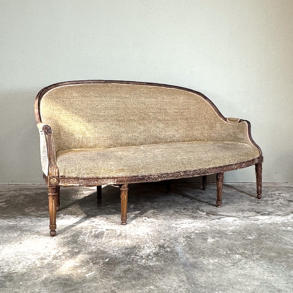 A mid-19th century French canape featuring a carved wooden frame with fluted legs and warm beige upholstery.