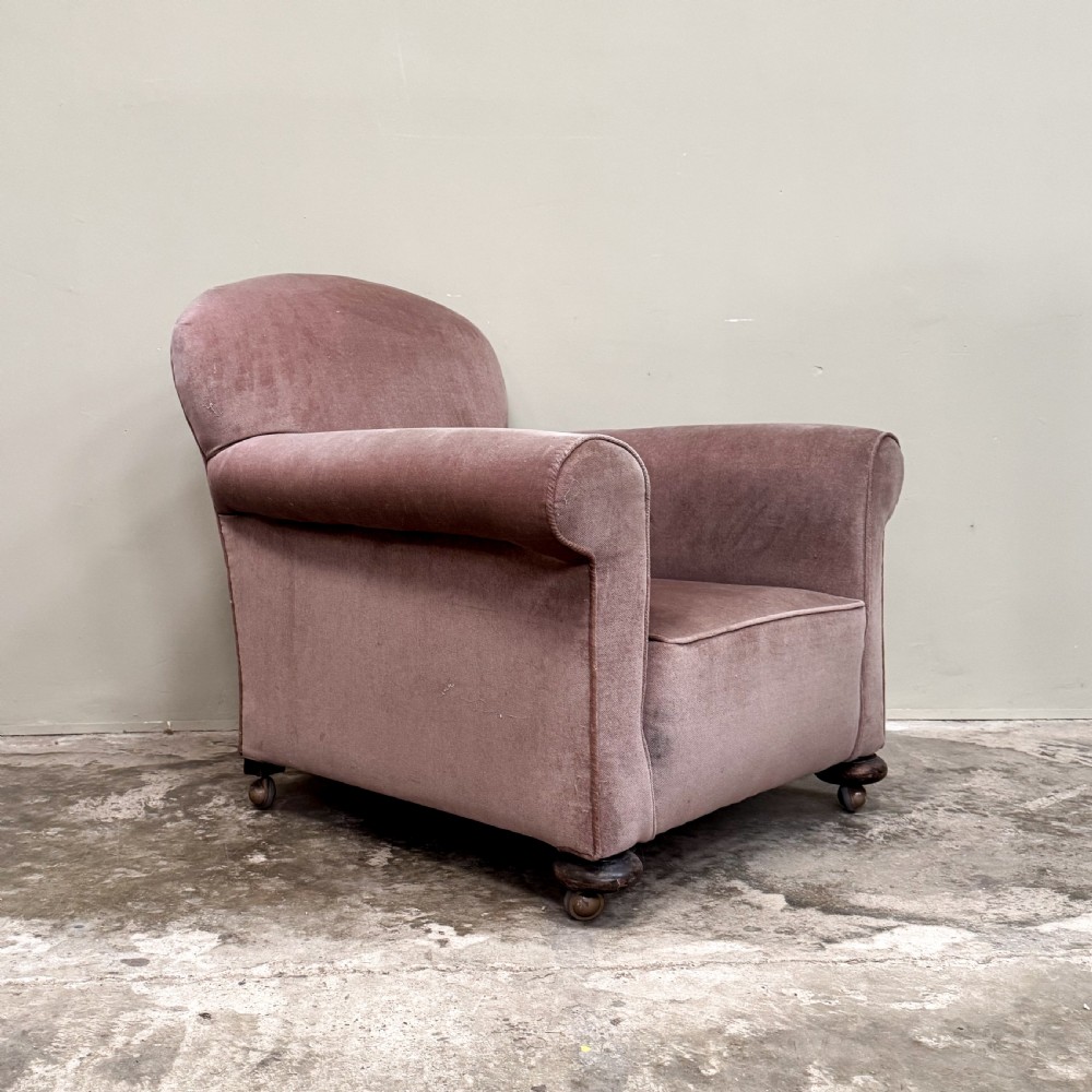 A 1930s upholstered armchair covered in dusty pink velvet with a curved back, rolled arms, and turned feet on castors.