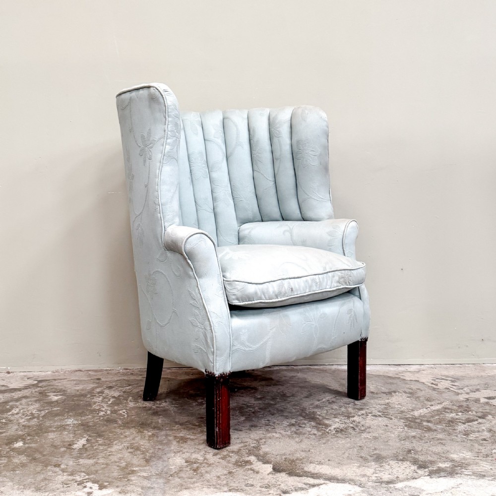A light blue 1920s ribbed barrel back armchair with floral fabric upholstery and square dark wood legs.