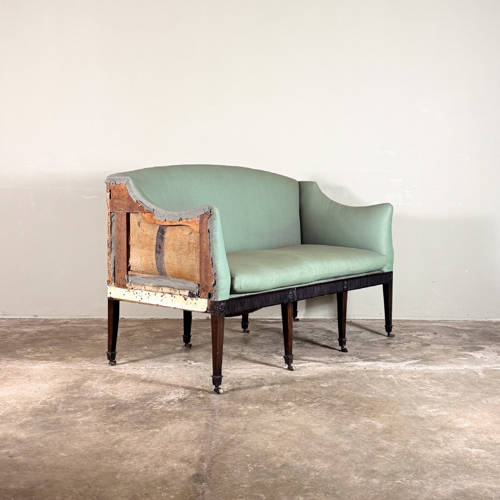 A Georgian two-seater sofa upholstered in light sage green fabric with a carved mahogany frame, fluted frieze, and tapered legs on brass castors. View II