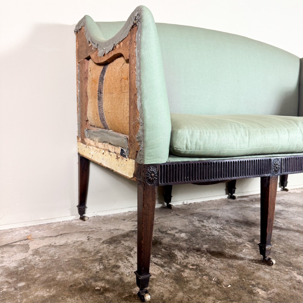 A Georgian two-seater sofa upholstered in light sage green fabric with a carved mahogany frame, fluted frieze, and tapered legs on brass castors. View III