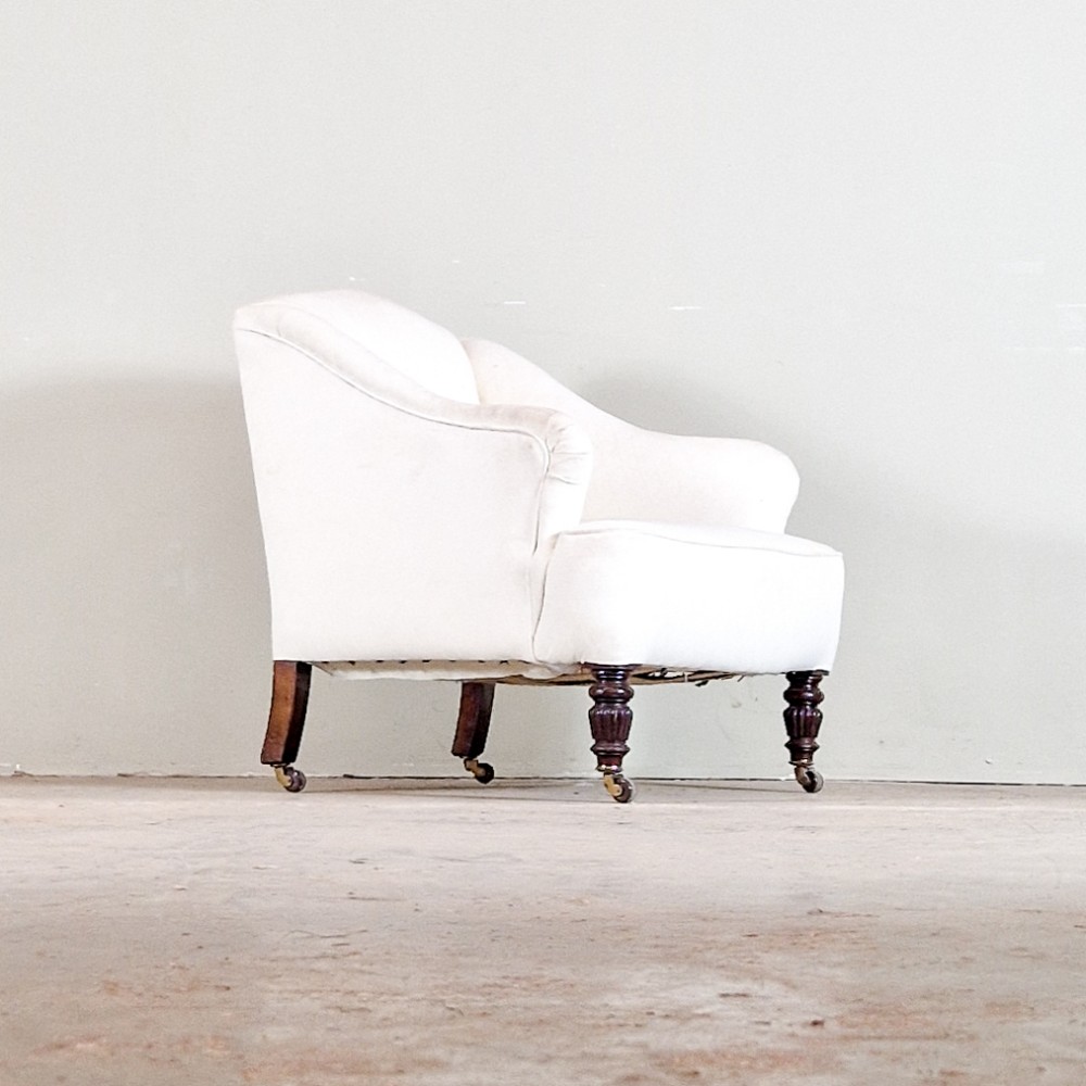A low-slung 19th-century petite armchair upholstered in plain cream fabric with turned dark mahogany front legs on brass castors.
