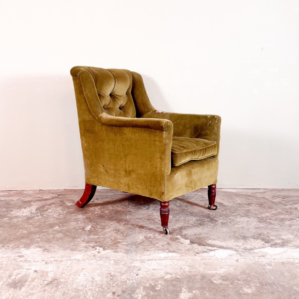 An antique Regency library armchair upholstered in olive green velvet with a buttoned backrest and turned mahogany front legs on brass castors.