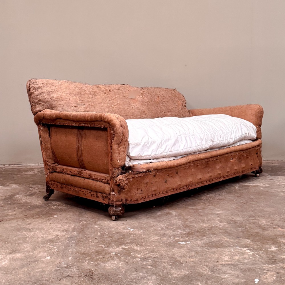 A 1930s three-seater sofa frame stripped down to its natural hessian lining with turned timber front legs on brass castors.