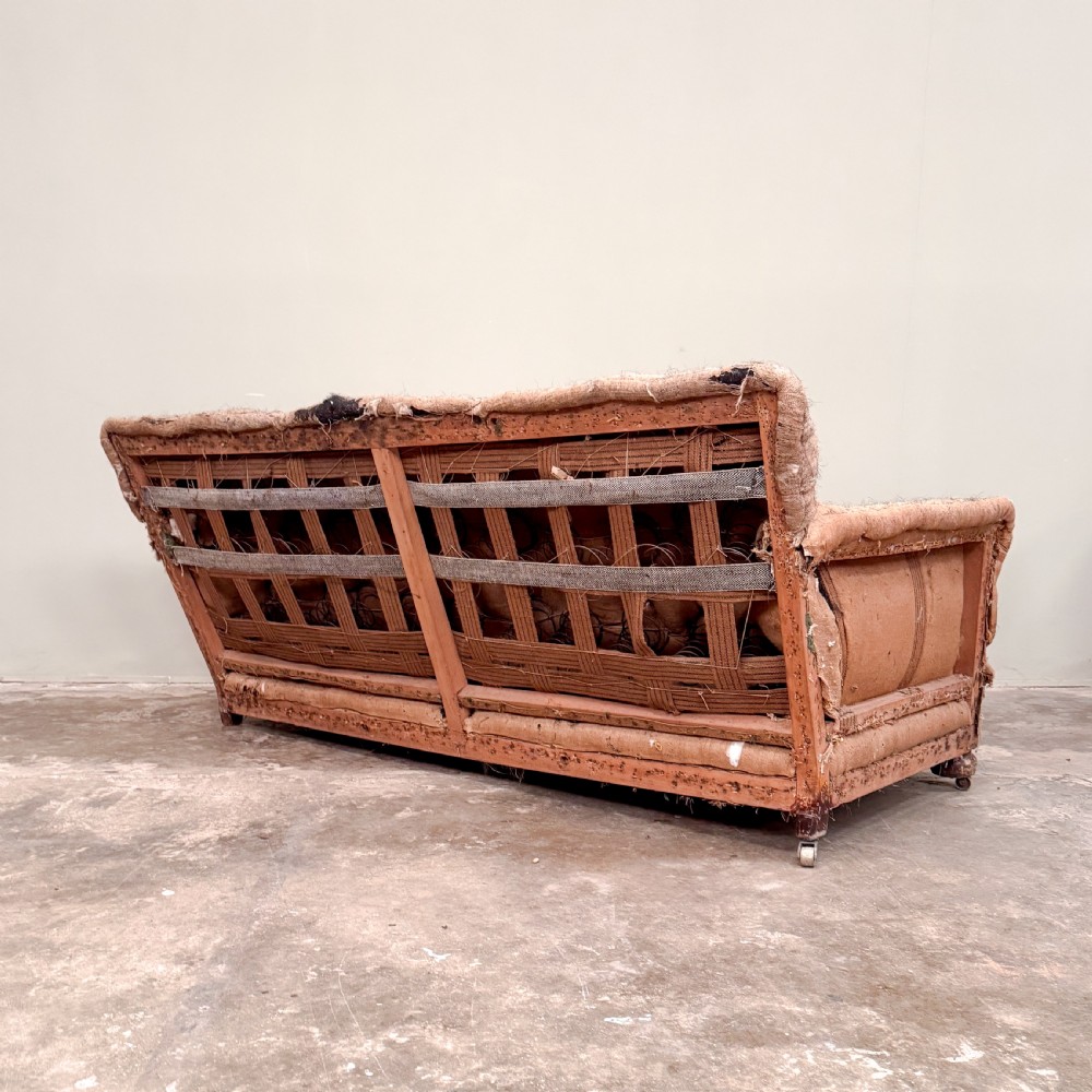 A 1930s three-seater sofa frame stripped down to its natural hessian lining with turned timber front legs on brass castors. View IV