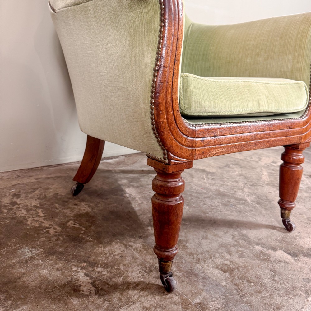 A Regency period library armchair upholstered in pale green velvet, featuring carved mahogany lyre-shaped arms and turned front legs on brass castors. View III