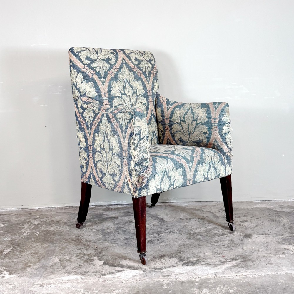 An Edwardian upholstered library armchair with damask patterned fabric in blue and pink, standing on tapered mahogany legs with brass castors. View II