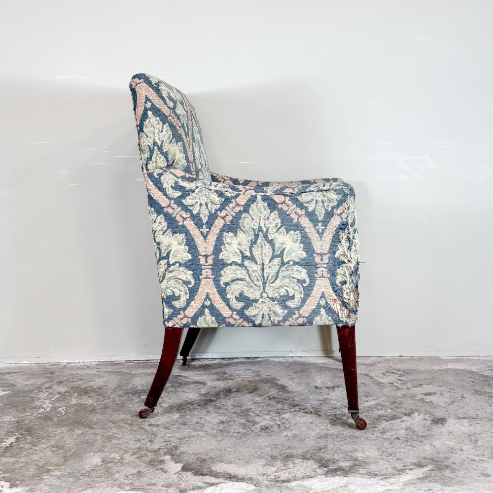 An Edwardian upholstered library armchair with damask patterned fabric in blue and pink, standing on tapered mahogany legs with brass castors. View III