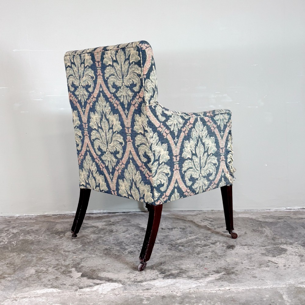 An Edwardian upholstered library armchair with damask patterned fabric in blue and pink, standing on tapered mahogany legs with brass castors. View IV