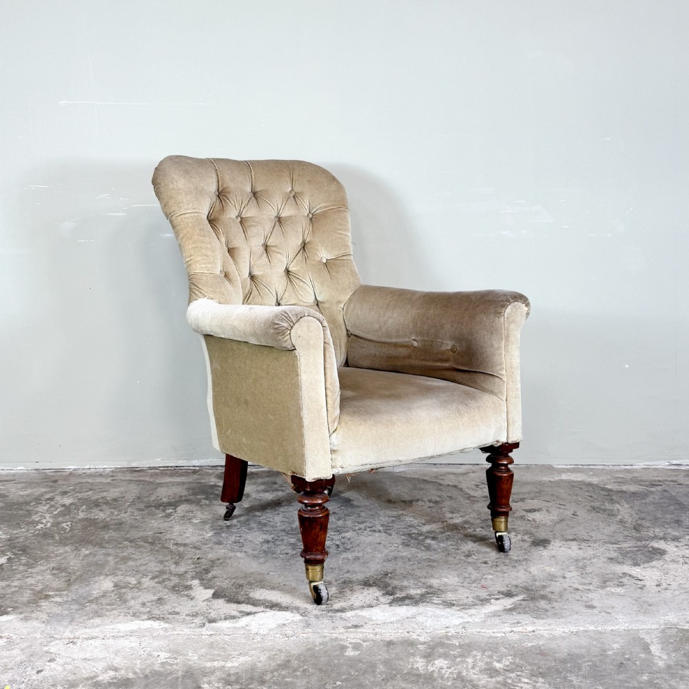 A nineteenth-century Victorian library armchair upholstered in beige velvet featuring a button-tufted backrest and turned mahogany legs with brass castors.