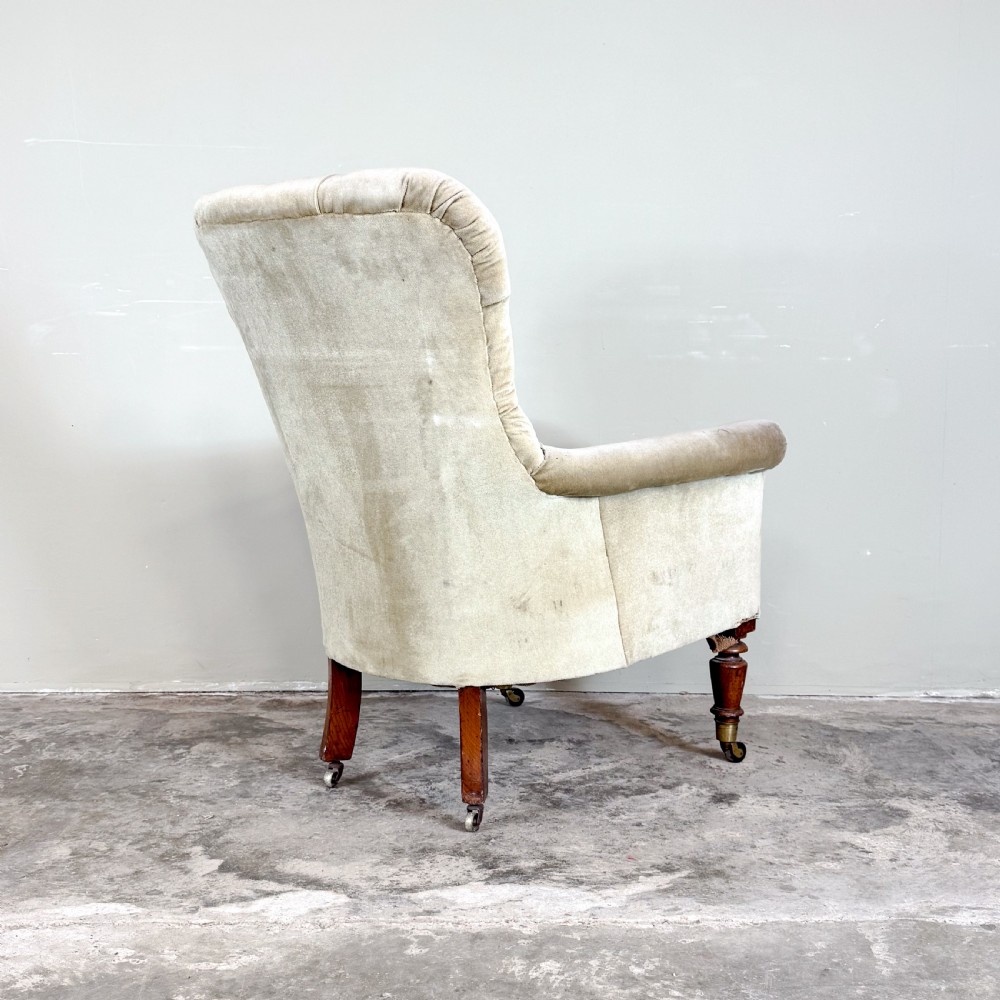 A nineteenth-century Victorian library armchair upholstered in beige velvet featuring a button-tufted backrest and turned mahogany legs with brass castors. View IV
