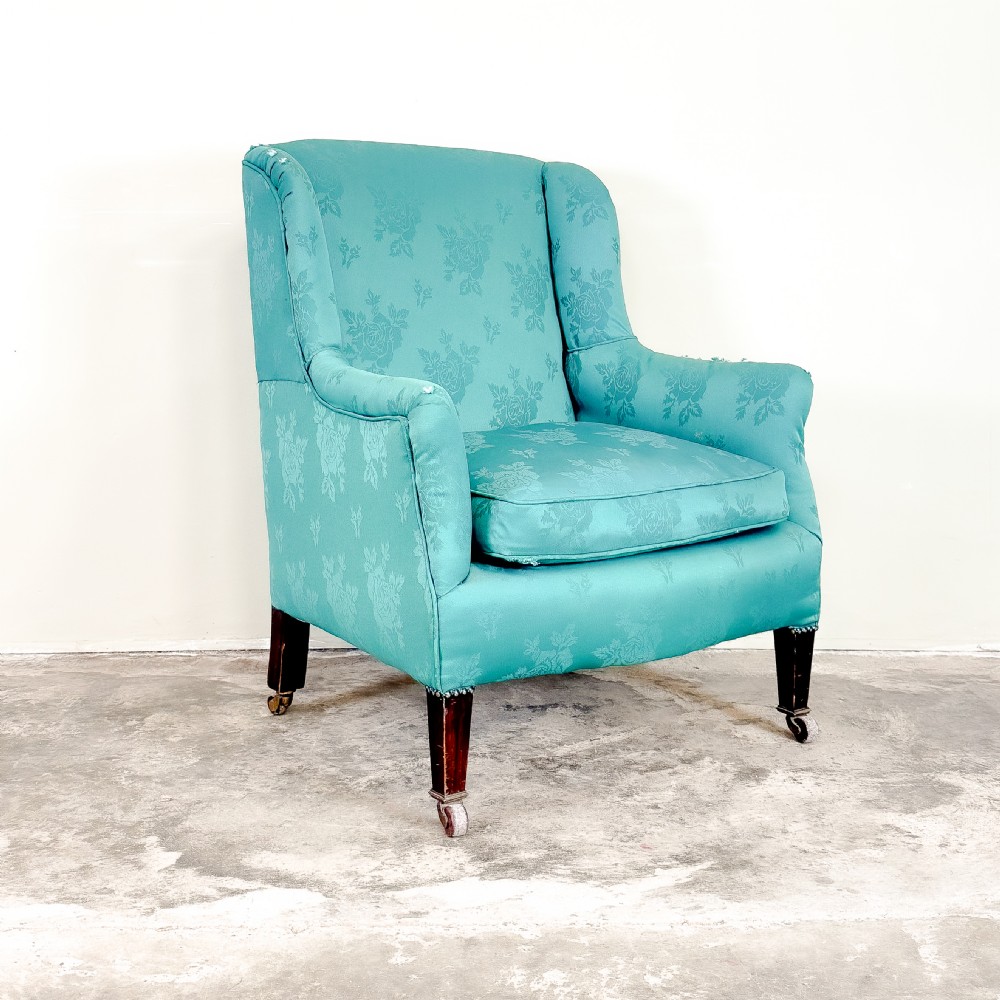 An Edwardian winged armchair upholstered in turquoise floral damask fabric, featuring square tapering legs on brass castors.