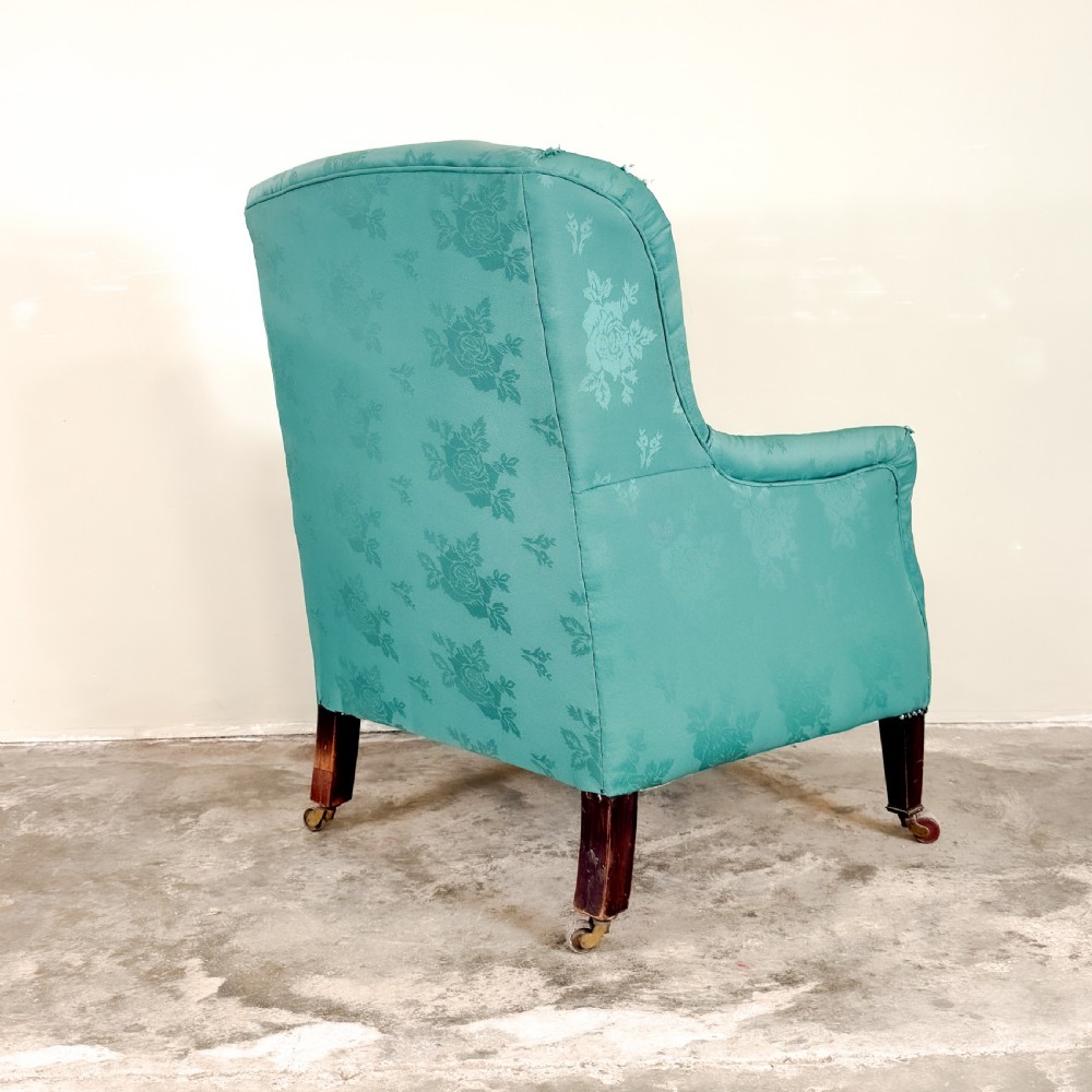 An Edwardian winged armchair upholstered in turquoise floral damask fabric, featuring square tapering legs on brass castors. View IV