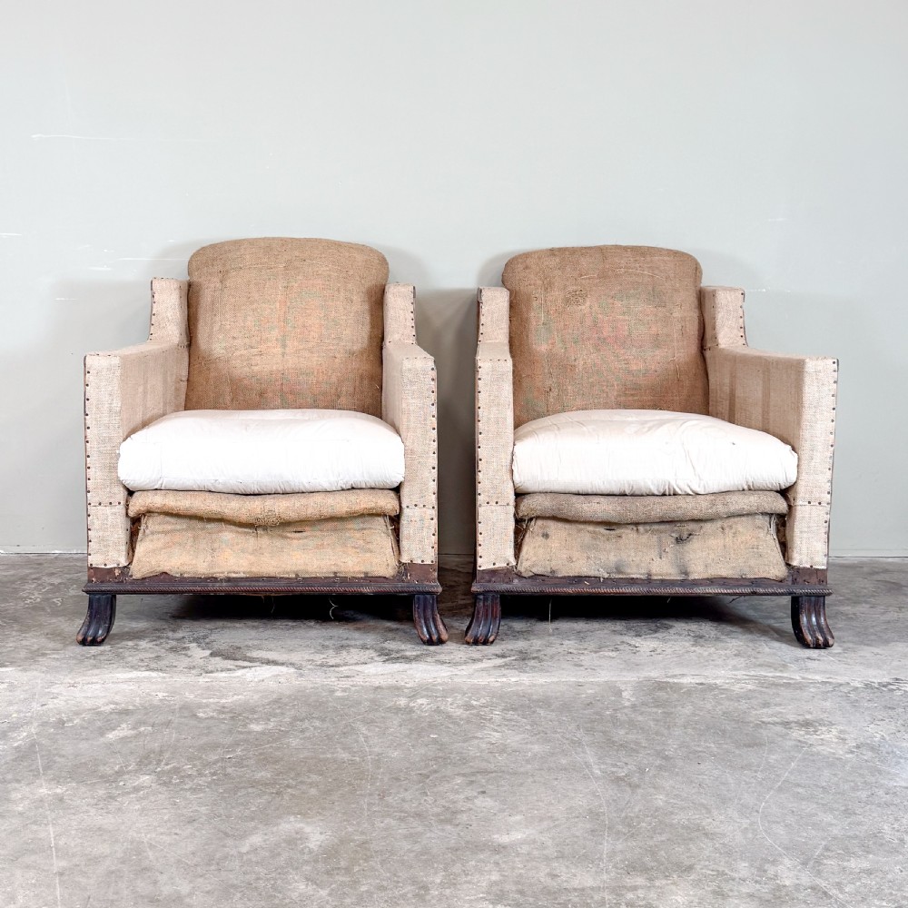 A pair of 1920s French armchairs upholstered in beige hessian with white seat cushions, stud trim, and carved dark wooden legs.