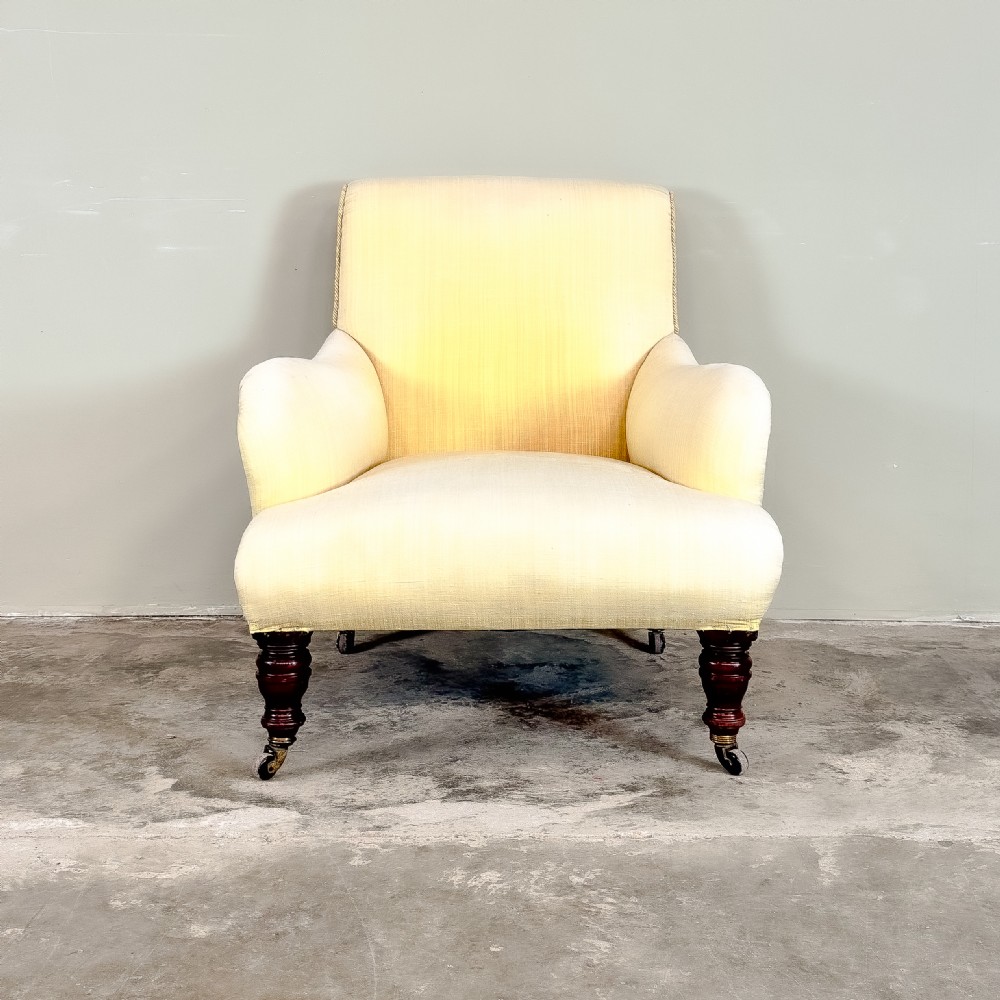 A 19th-century upholstered armchair featuring pale yellow fabric, padded P-shaped arms, and dark turned mahogany legs on brass castors.