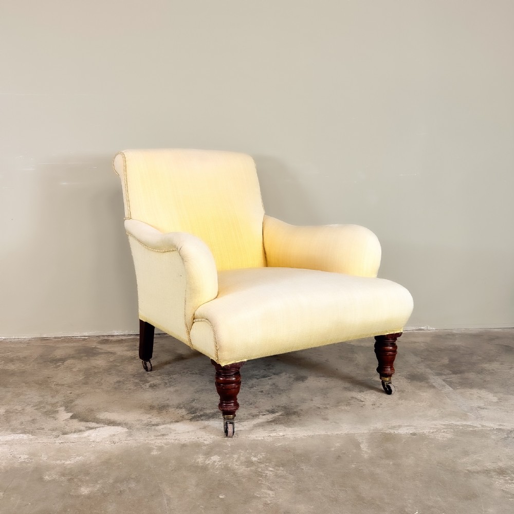 A 19th-century upholstered armchair featuring pale yellow fabric, padded P-shaped arms, and dark turned mahogany legs on brass castors. View II